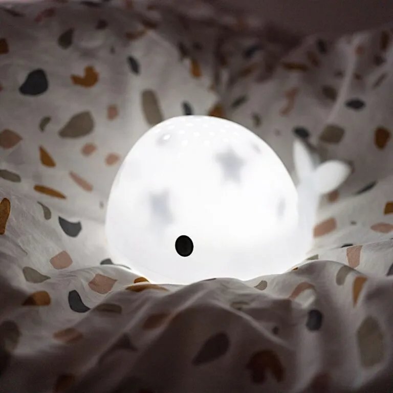 Lampe en forme de boule translucide émettant une lumière douce posée sur des draps imprimés colorés, ambiance paisible et cosy.